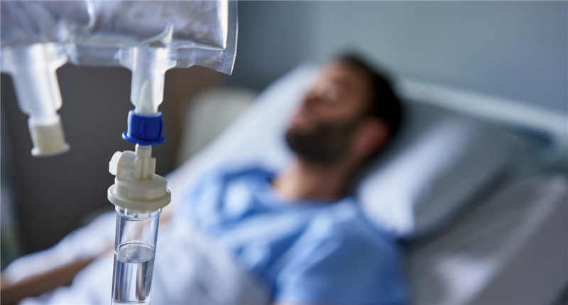 A man lies in a hospital bed receiving an IV drip.