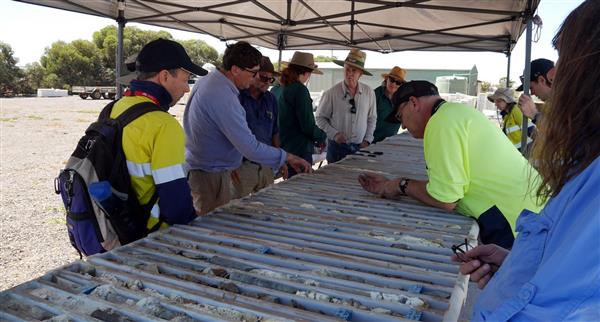 Several Lincoln Metals workers gathered around steel bars on a table.