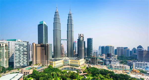 An image of the capital city of Malaysia taken from a distance with two large towers identical in height standing in front of a green park space
