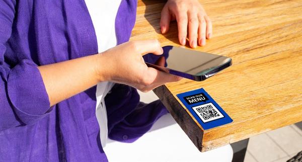 A woman in a purple jumper scans in QR code on a wooden table.